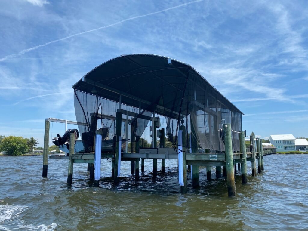 Boat lift cover installed over a dock on a sunny day, protecting a watercraft on a coastal property.